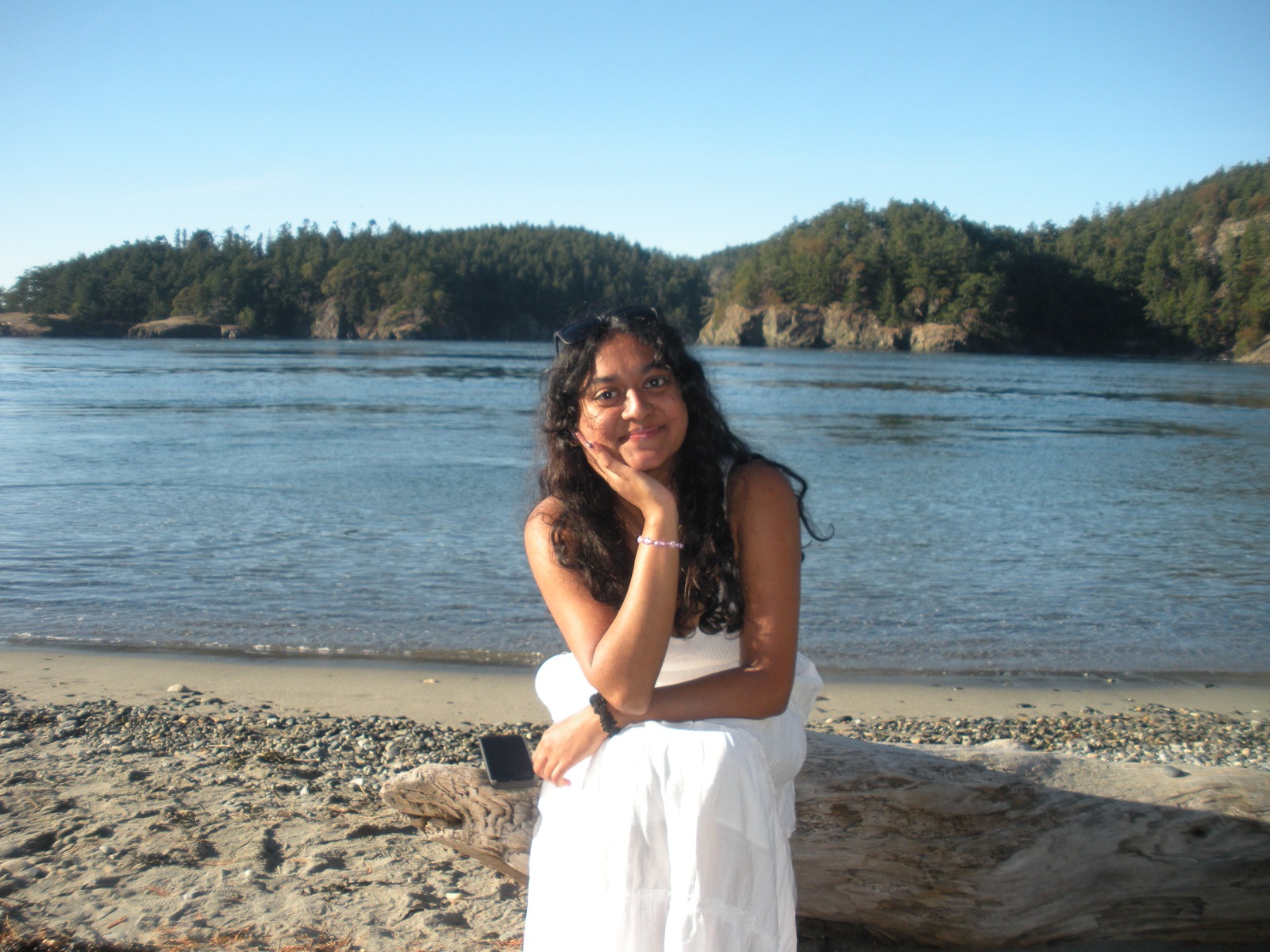 Ruthu sitting on a log on the beach, staring at the camera